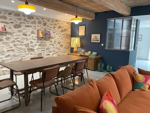 A dining area with a wooden table and chairs, a stone wall, and a sofa with colorful cushions. - The Domaine de la Feuilleraie (Montséret)