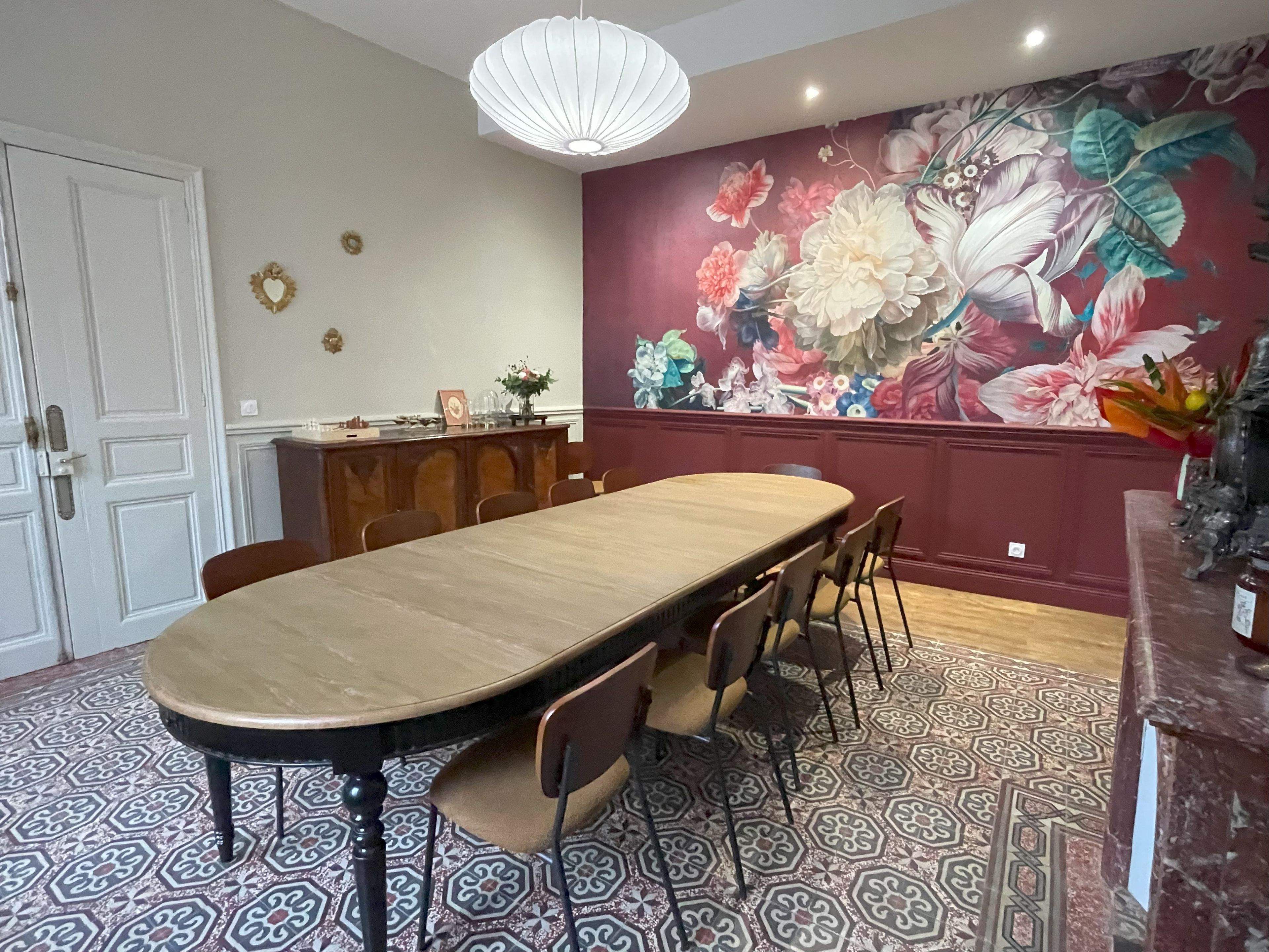 Uma sala de jantar com uma mesa comprida, cadeiras, um painel decorativo e um chão estampado.