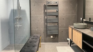 A modern bathroom with a glass-enclosed shower, a bench, a towel rack, and a sink with a mirror. - Vrbo Property (Montséret)