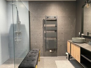 Een moderne badkamer met een douchecabine van glas, een bankje, een handdoekrek en een wastafel met spiegel.