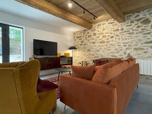 A living room with a stone wall, a sofa, a television, and a lamp. - The Domaine de la Feuilleraie   (Montséret)