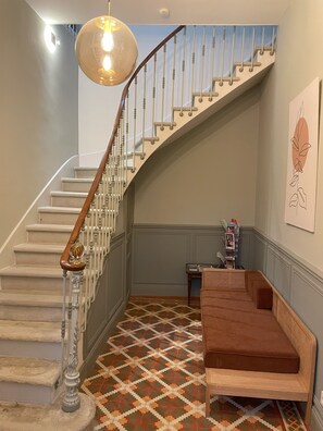 A staircase with a wooden handrail and white balusters, leading to a landing with a patterned floor and a brown cushioned bench. - The Domaine de la Feuilleraie   (Montséret)