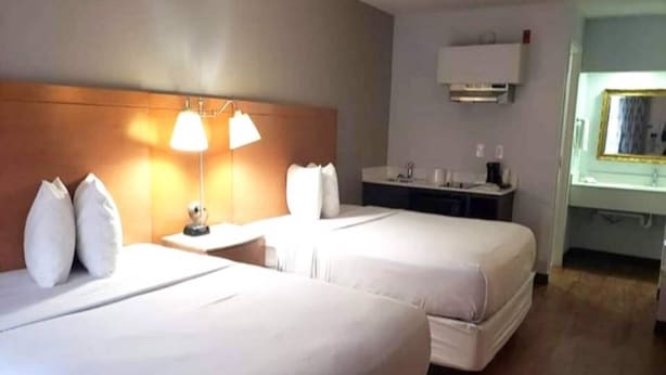 A hotel room with two beds, a bedside table with lamps, a small desk, and a mirror. - 2 Queen Beds | Suite, Non-Smoking, Micfridge (Savannah GA)