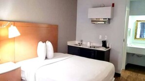 A hotel room with a bed, a bedside table, a lamp, a small kitchenette with a sink, and a mirror. - 1 King Bed | Non-Smoking, Micfridge (Savannah GA)