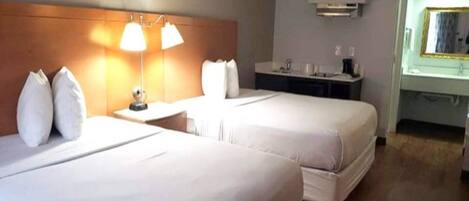 A hotel room with two beds, a nightstand, a lamp, a mirror, and a small table.