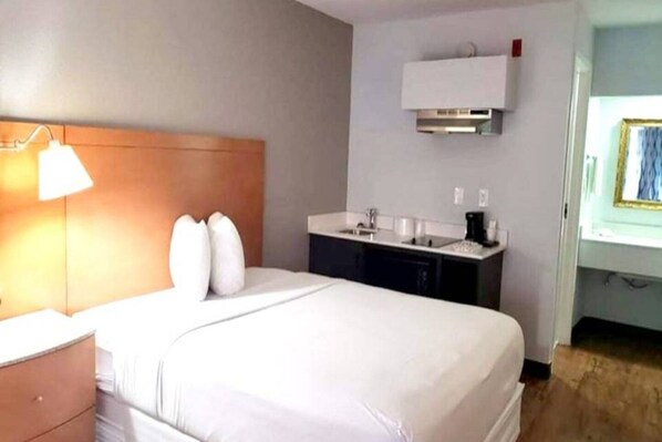Habitación de hotel con cama, mesita de noche, lámpara y una pequeña cocina con lavabo y encimera.