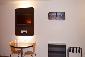 A small room with a round table, two chairs, a television mounted on the wall, and a coat rack. - 1 King Bed | Non-Smoking, Micfridge (KINGSLAND)