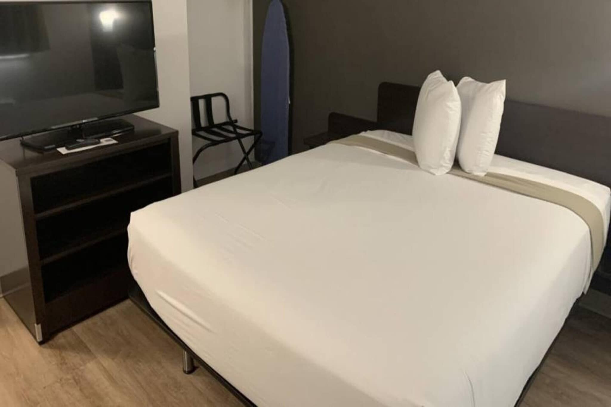 Una habitación de hotel con cama, televisor sobre un mueble, una silla y una tabla de surf.