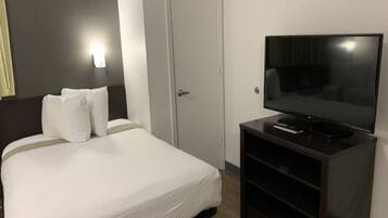 A hotel room with a bed, a television on a stand, and a door.
