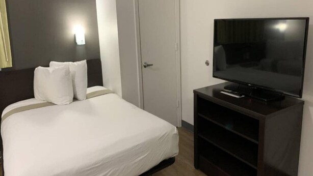 Et hotelværelse med en seng, et fjernsyn på et stativ og en dør.