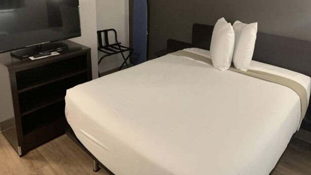 A hotel room with a bed, a TV on a stand, a chair, and a surfboard. - 1 Queen Bed|Smoking, Kitchen (Hampton)