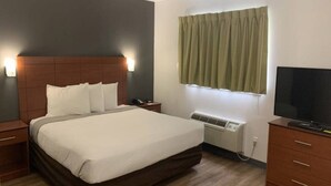 A hotel room with a bed, bedside tables, a TV, an air conditioning unit, and a window with curtains. - 1 Queen Bed|Smoking, Kitchen (Hampton)
