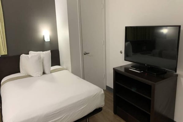 Une chambre d’hôtel avec un lit, un téléviseur posé sur un meuble et une porte.