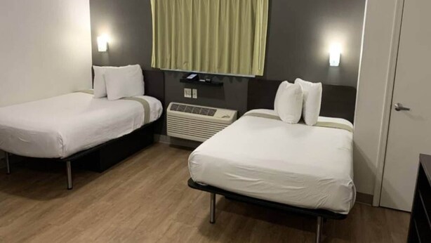 Et hotelværelse med to senge, en varmeblæser, et lille bord og et skab.
