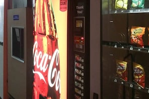 Una máquina expendedora con el logo de Coca-Cola, un cartel que dice 'Gracias' y aperitivos como Cheetos y Pringles.