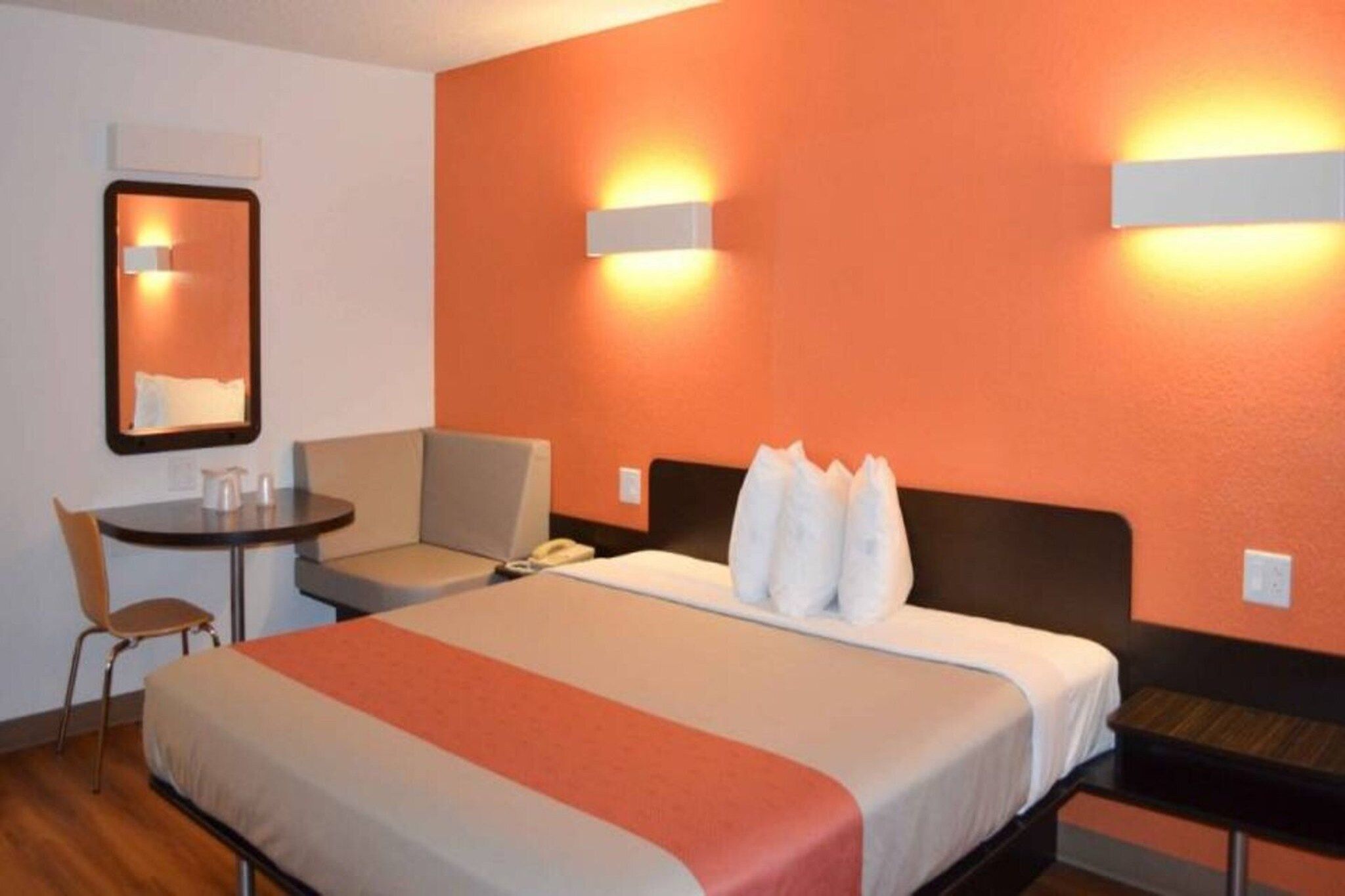 A hotel room with a bed, a desk, a chair, and two wall-mounted lamps.