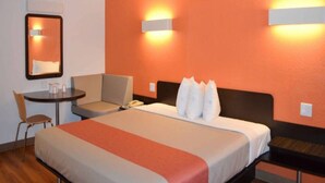 Hotellihuone, jossa on sänky, työpöytä, tuoli ja kaksi seinään kiinnitettyä lamppua.