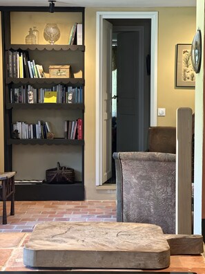 Uma sala de estar aconchegante com uma estante, uma poltrona estampada e uma mesa de centro de madeira.