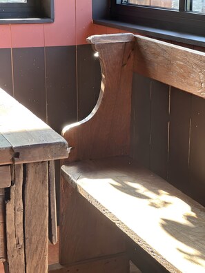 A wooden bench with a curved backrest and a slatted seat, positioned next to a window with a view of the outside.