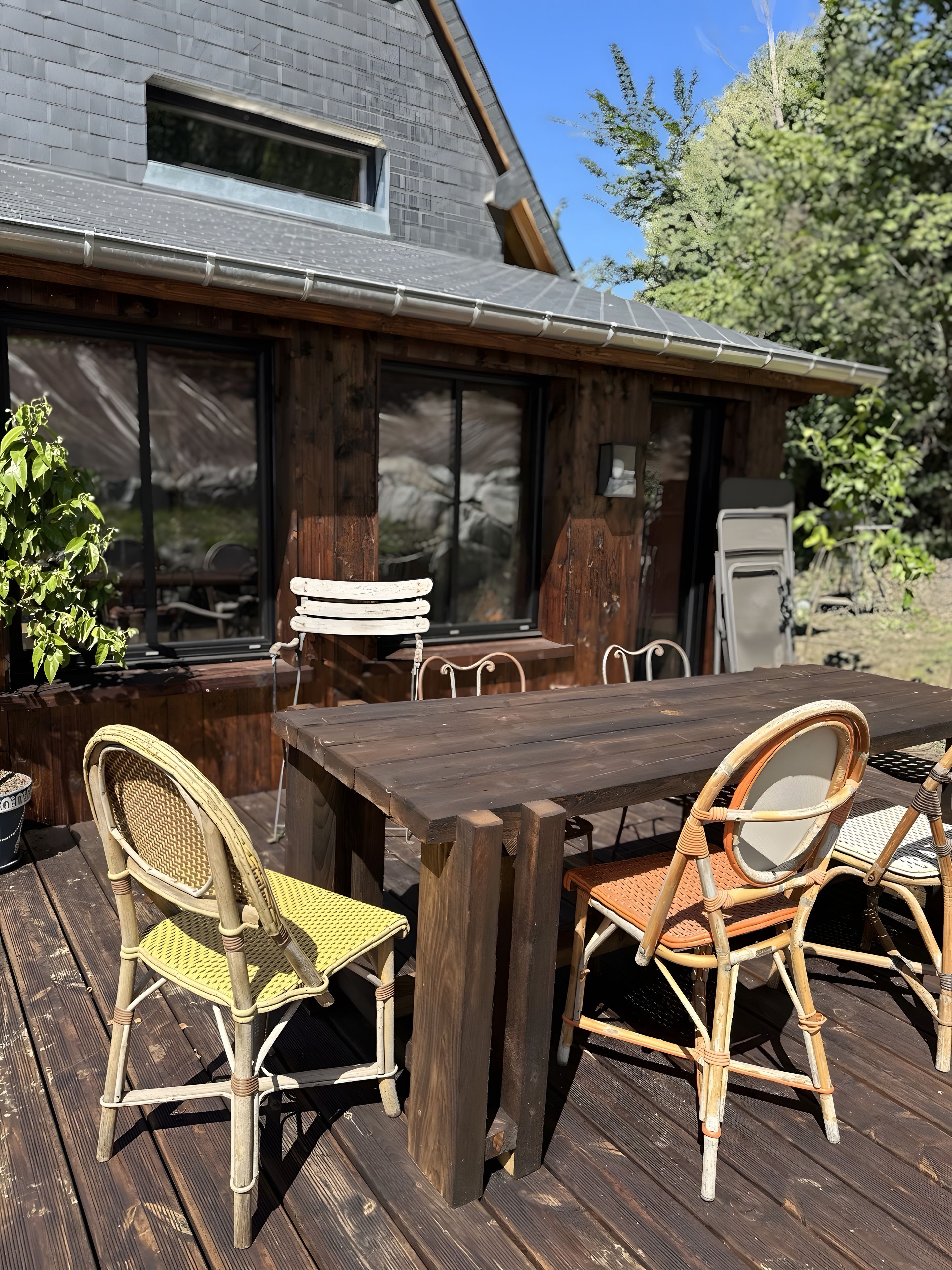 Una terrazza esterna in legno con tavolo e sedie in vimini, una finestra e una porta che dà su un'area coperta.