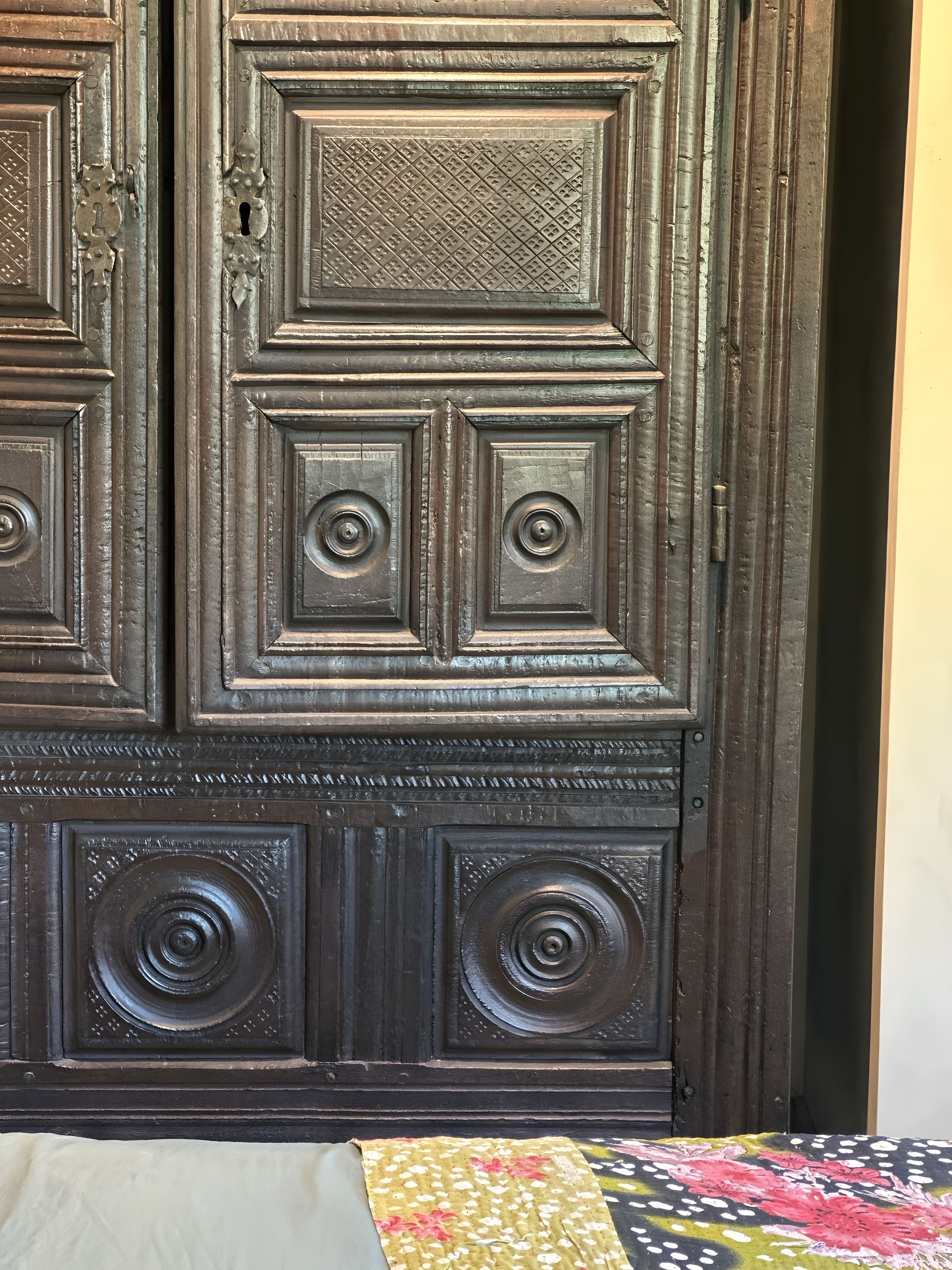 Une porte en bois sombre, ornée de sculptures complexes et dotée d’une poignée circulaire.