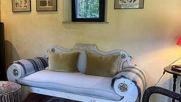 A room with a white sofa, a patterned armchair, a small round table, and a window with a view of greenery.