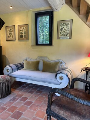 A room with a white sofa, a patterned armchair, a small round table, and a window with a view of greenery.
