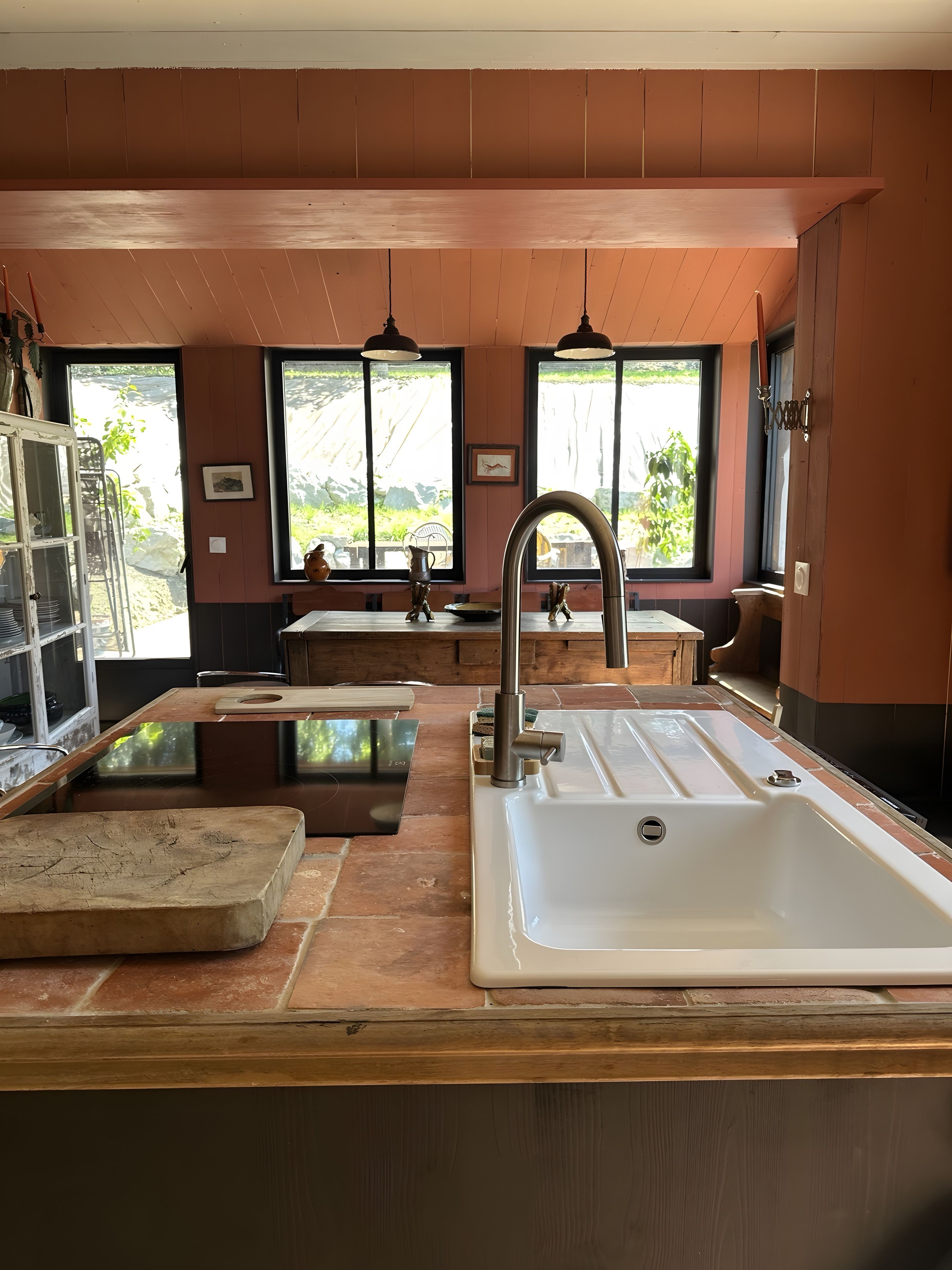 Cozinha com uma pia grande, bancadas de madeira e vista para o verde pelas janelas.