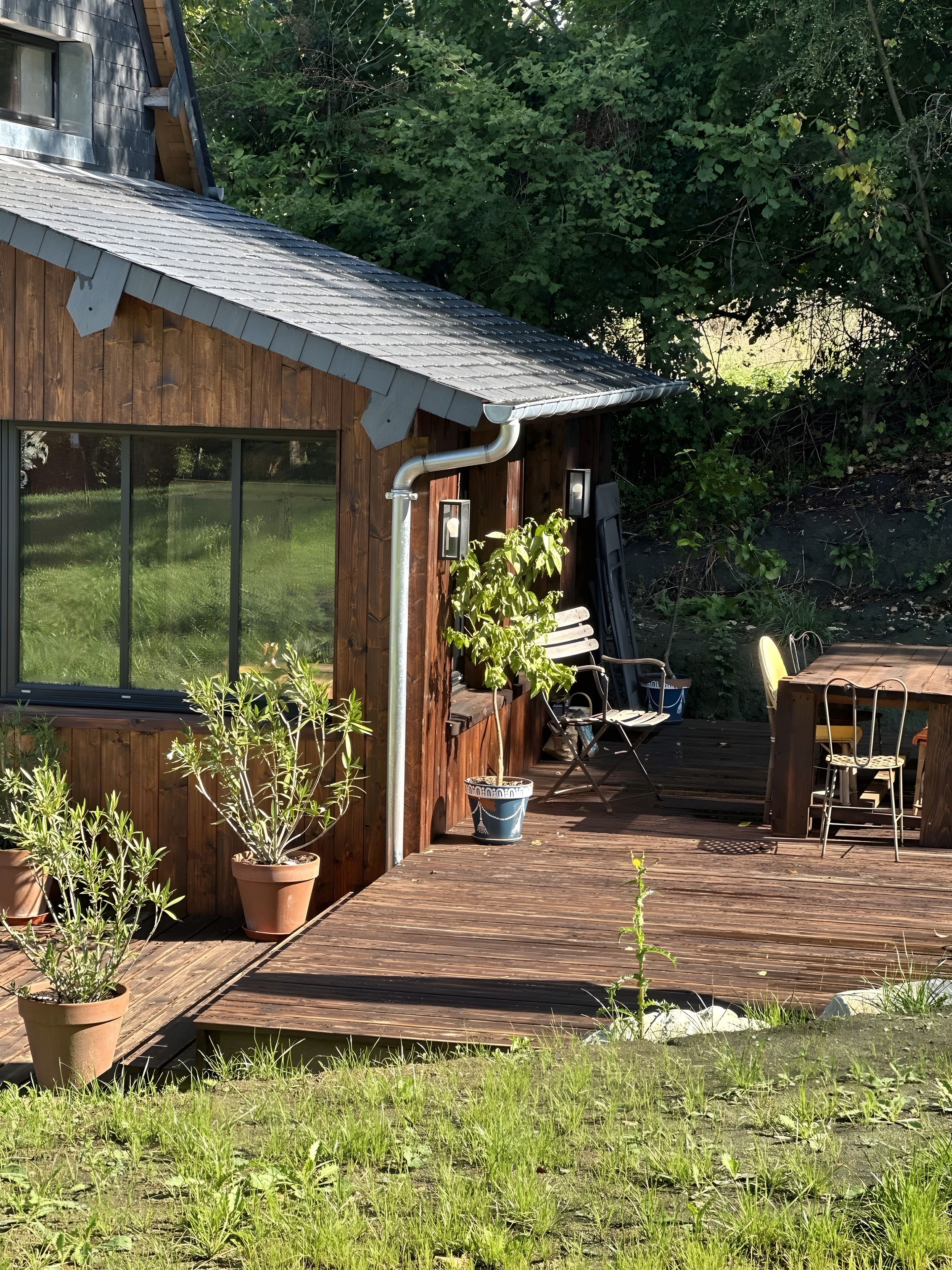 A wooden cabin with a deck, potted plants, and outdoor furniture.