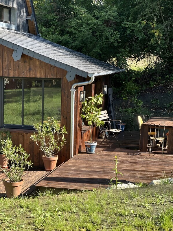Uma cabana de madeira com varanda, plantas em vasos e mobiliário de exterior.