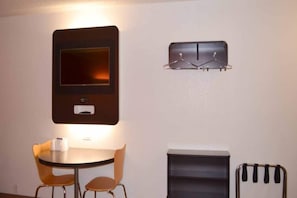 A small room with a round table, two chairs, a TV mounted on the wall, and a shelf with two items. - 2 Queen Beds | Non-Smoking, Micfridge (KINGSLAND)