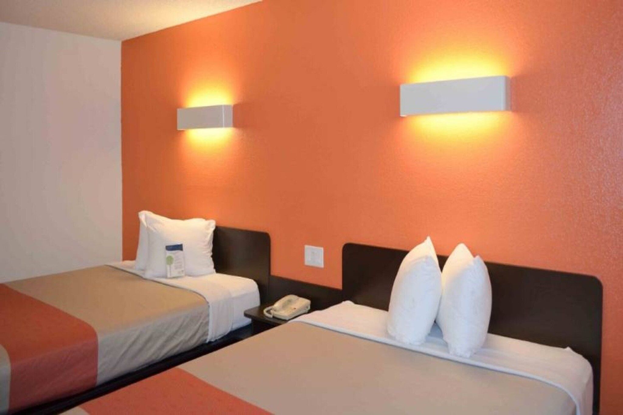 Une chambre d’hôtel avec deux lits, chacun doté de draps et d’oreillers blancs, une table de chevet avec un téléphone et des lampes fixées au mur.