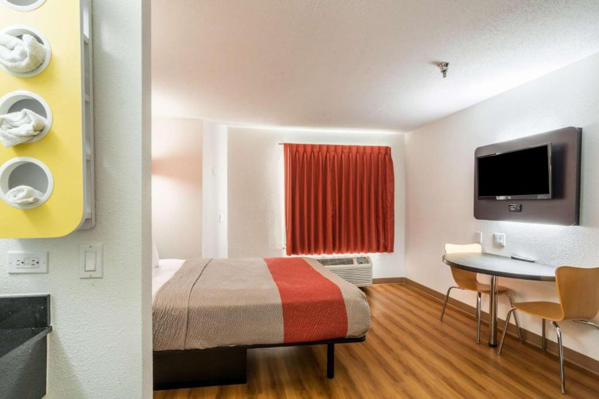 A hotel room with a bed, a desk, a television, and a window with curtains.