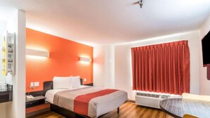 Habitació d'hotel amb llit, taula de nit i cortina vermella.