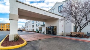 Entrada d'hotel amb un passadís cobert, un aparcament i un edifici amb nombroses finestres.