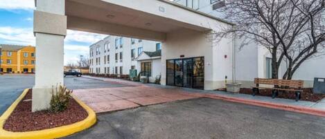 A hotel entrance with a covered walkway, a parking lot, and a building with multiple windows.