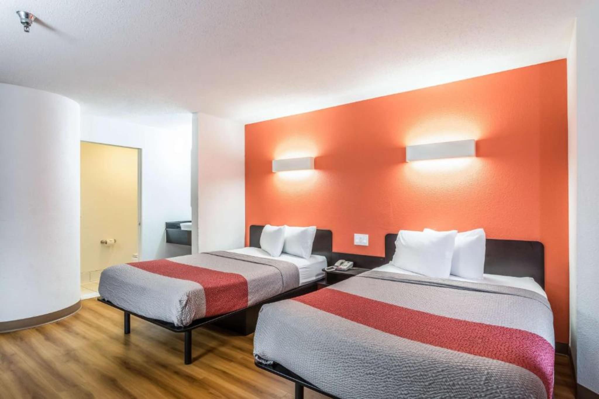 Ein Hotelzimmer mit zwei Betten, Holzboden und einer roten Wand als Blickfang.