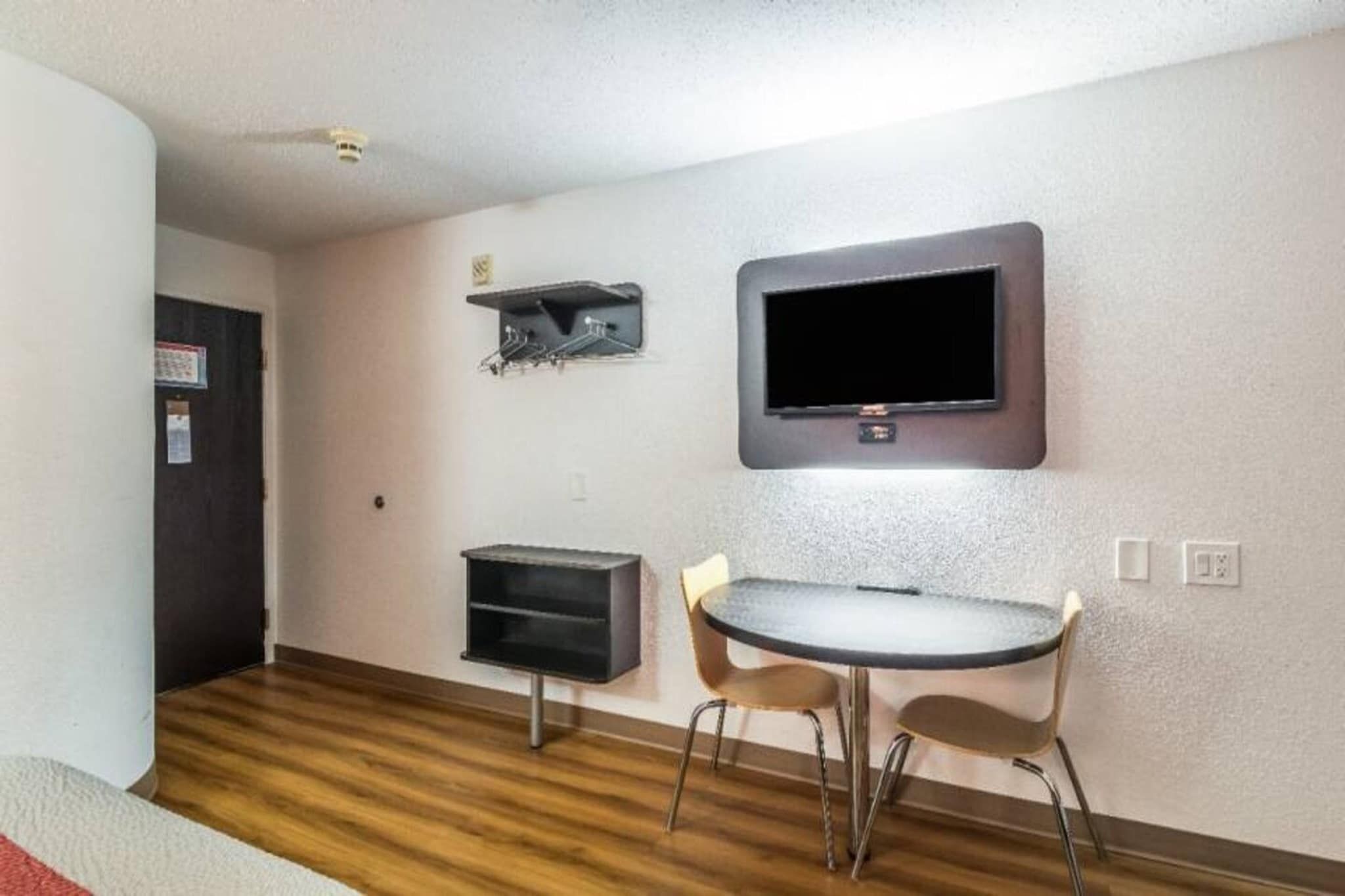 A small room with a flat-screen TV mounted on the wall, a small table with two chairs, and a wooden floor.