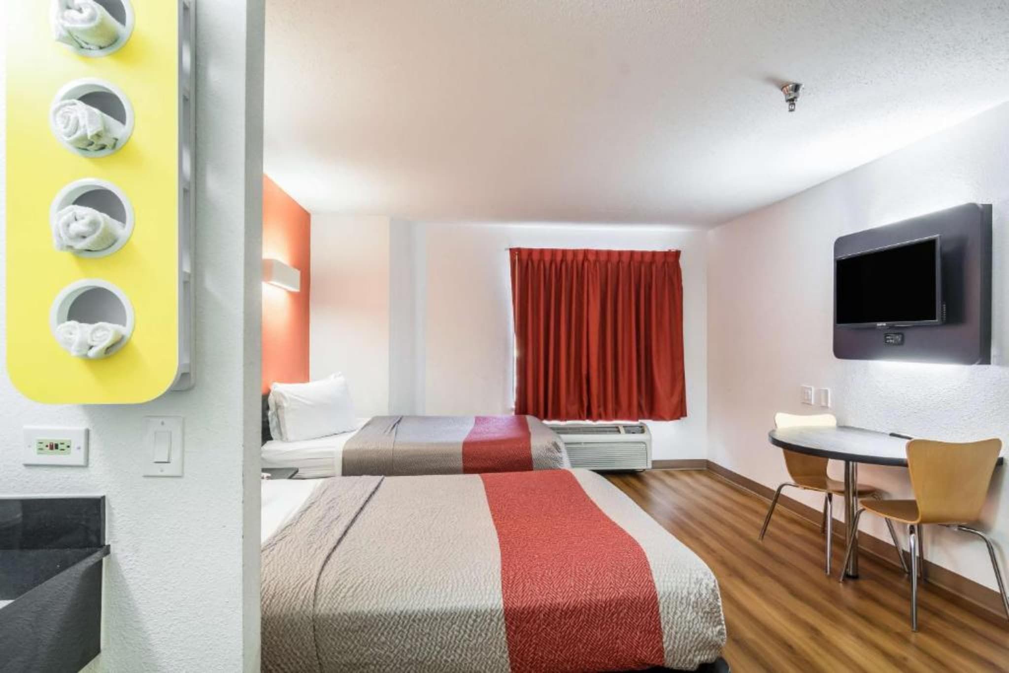 A hotel room with two beds, a desk, a chair, a TV, and a window with curtains.