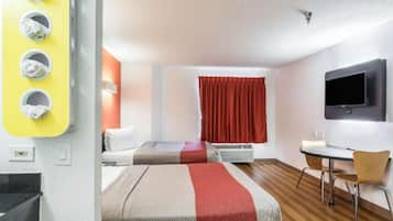 A hotel room with two beds, a desk, a chair, a TV, and a window with curtains.