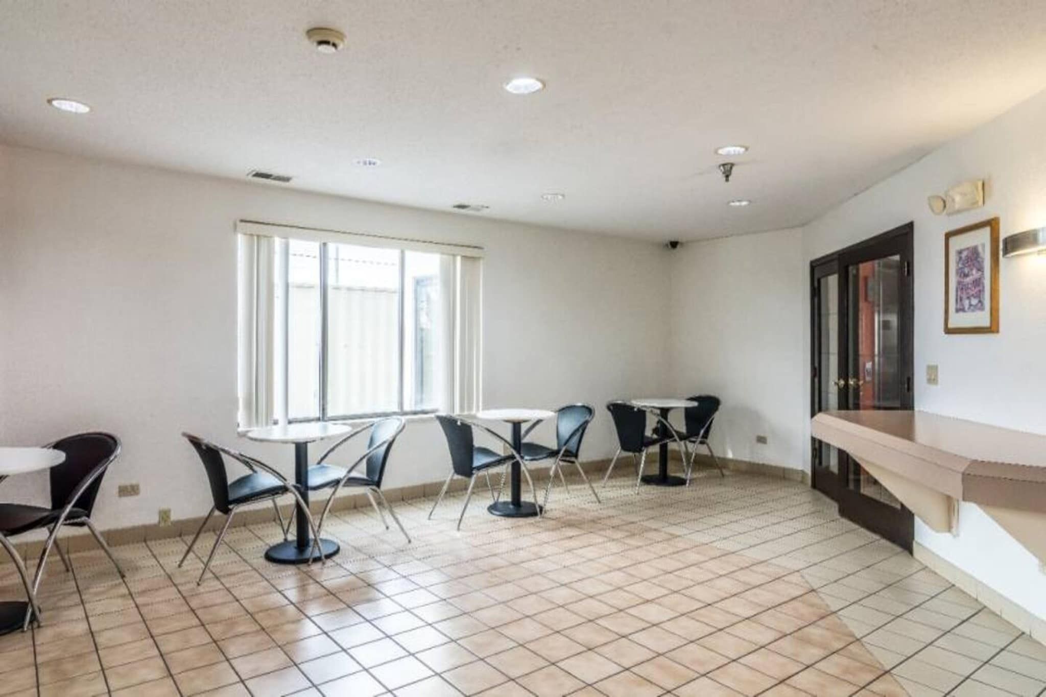 Ein Zimmer mit großem Fenster, Fliesenboden und einer Sitzecke mit Tischen und Stühlen.
