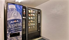 A water vending machine with a large Aquafina advertisement and a snack vending machine next to it.