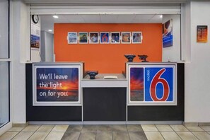 A reception desk with a clock, a sign reading 'We'll leave the light on for you.', and a 'motel 6' sign. - 1 Full Bed | ADA/RI Shower (Orlando FL)