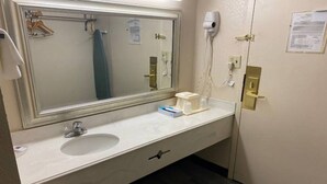 Casa de banho de hotel com um espelho grande, uma pia, um porta-toalhas, um secador de cabelo e um papel na parede.
