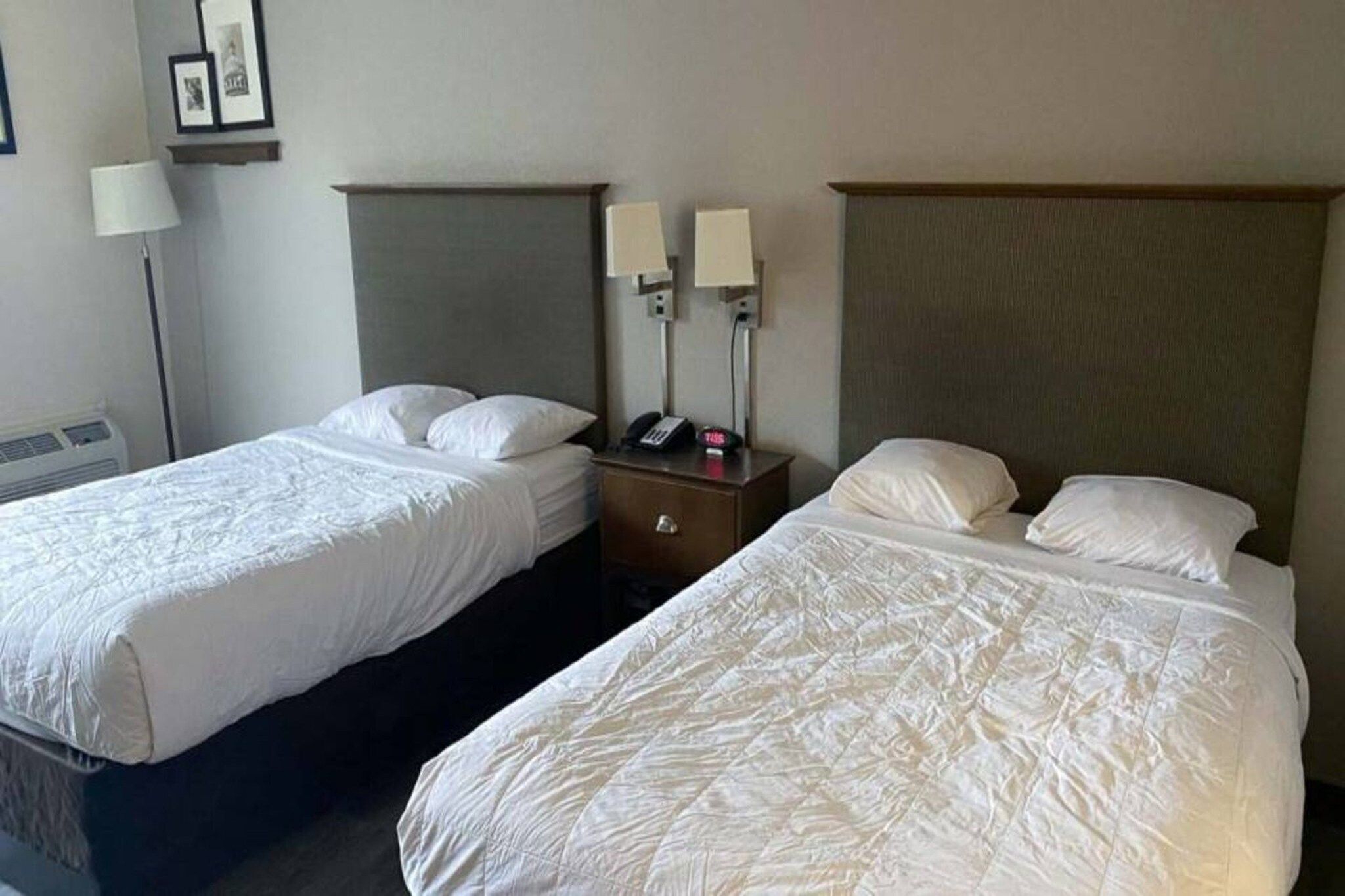 Twee enkele bedden met hoofdborden, een nachtkastje met een lamp en een aan de muur bevestigde telefoon.