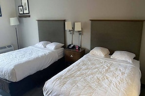 Twee enkele bedden met hoofdborden, een nachtkastje met een lamp en een aan de muur bevestigde telefoon.
