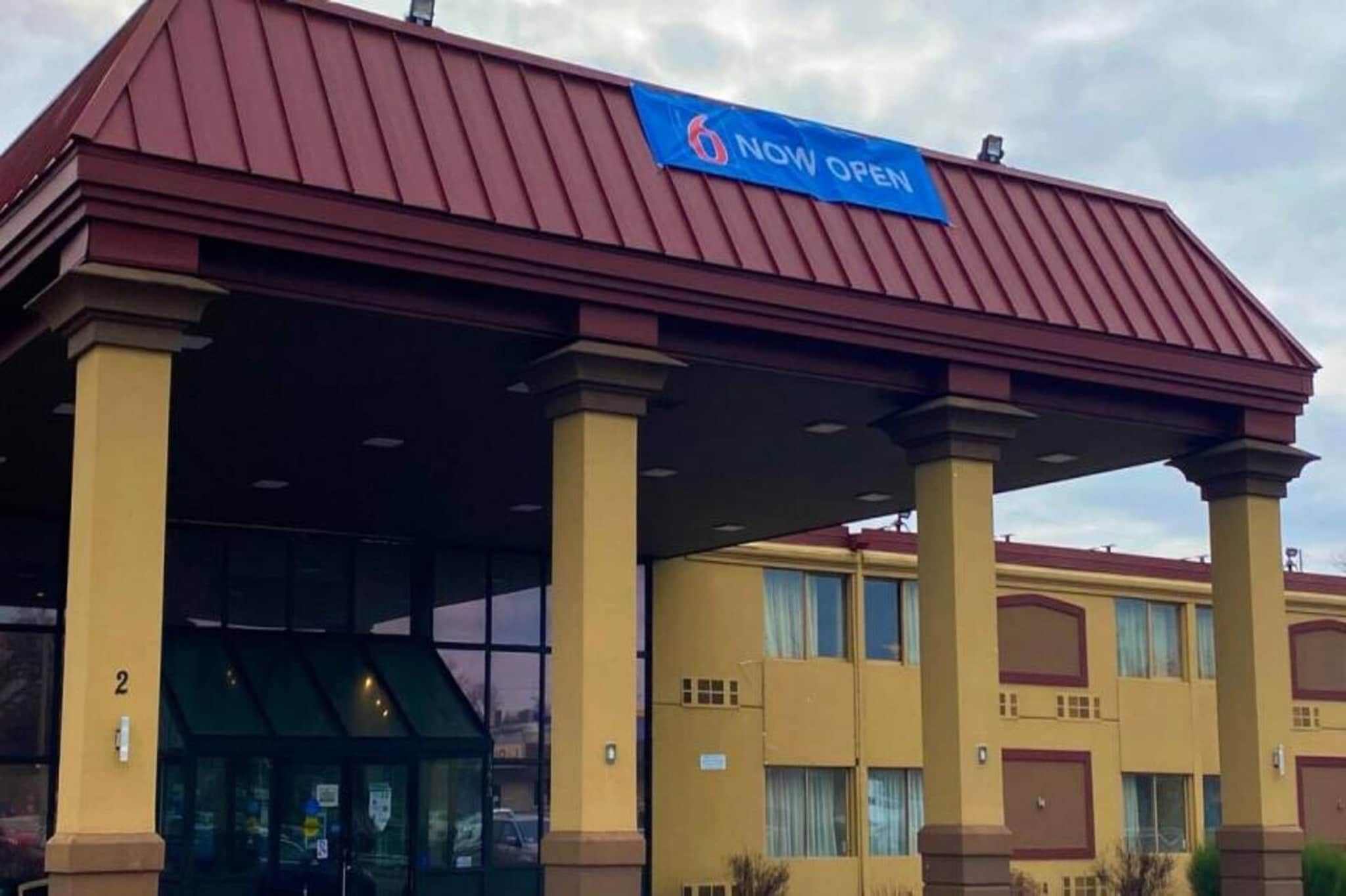 Een hotel met een 'NU OPEN' bord, een overdekte ingang en het nummer '2' op het gebouw.