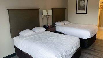 A hotel room with two single beds, a nightstand, a wall-mounted lamp, and a framed picture.