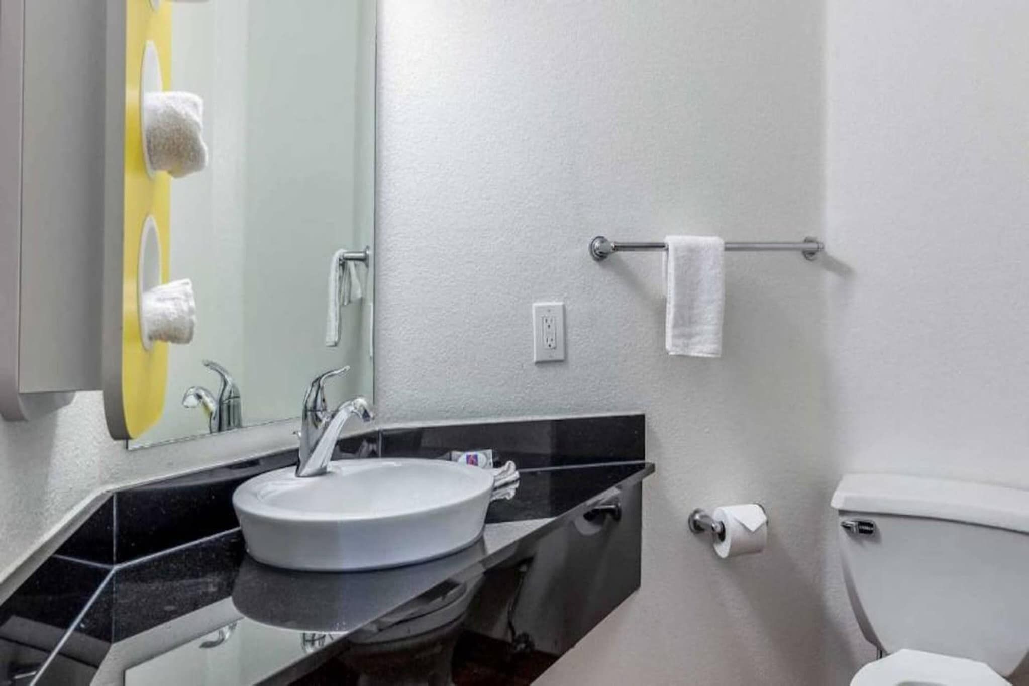 A bathroom with a sink, mirror, towel rack, toilet, and a towel hanging on the wall.