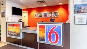 Een hotel receptiebalie met een groot nummer 6 bord, een digitale klok en een flatscreen televisie aan de muur.